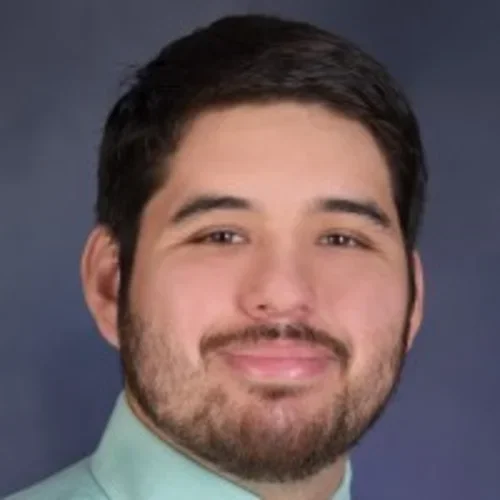 Headshot of Miguel Cuevas smiling with a gray background.
