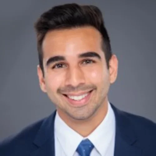 Headshot of Neal Dexit smiling with a gray background.