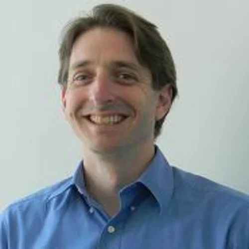 Headshot of David Elashoff smiling with a blue shirt and a beige background
