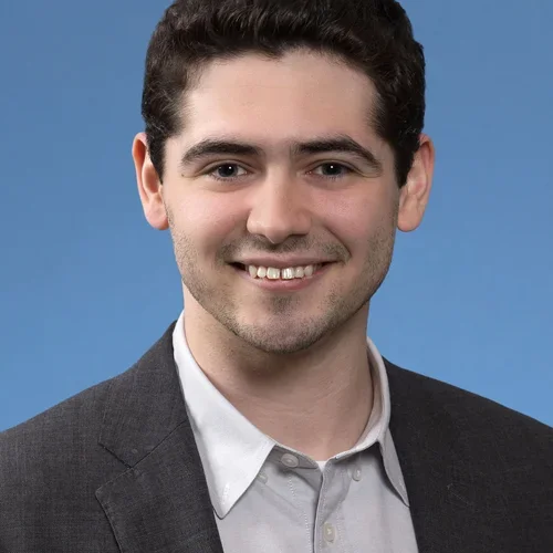 Headshot of William Turner smiling with a blue background.