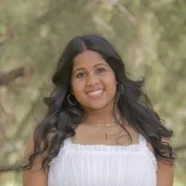 Sameera smiling in a white dress with a forest background